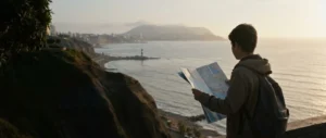 Un estudiante de espaldas mira un mapa de papel en el malecón de Barranco, frente al mar de Lima al atardecer